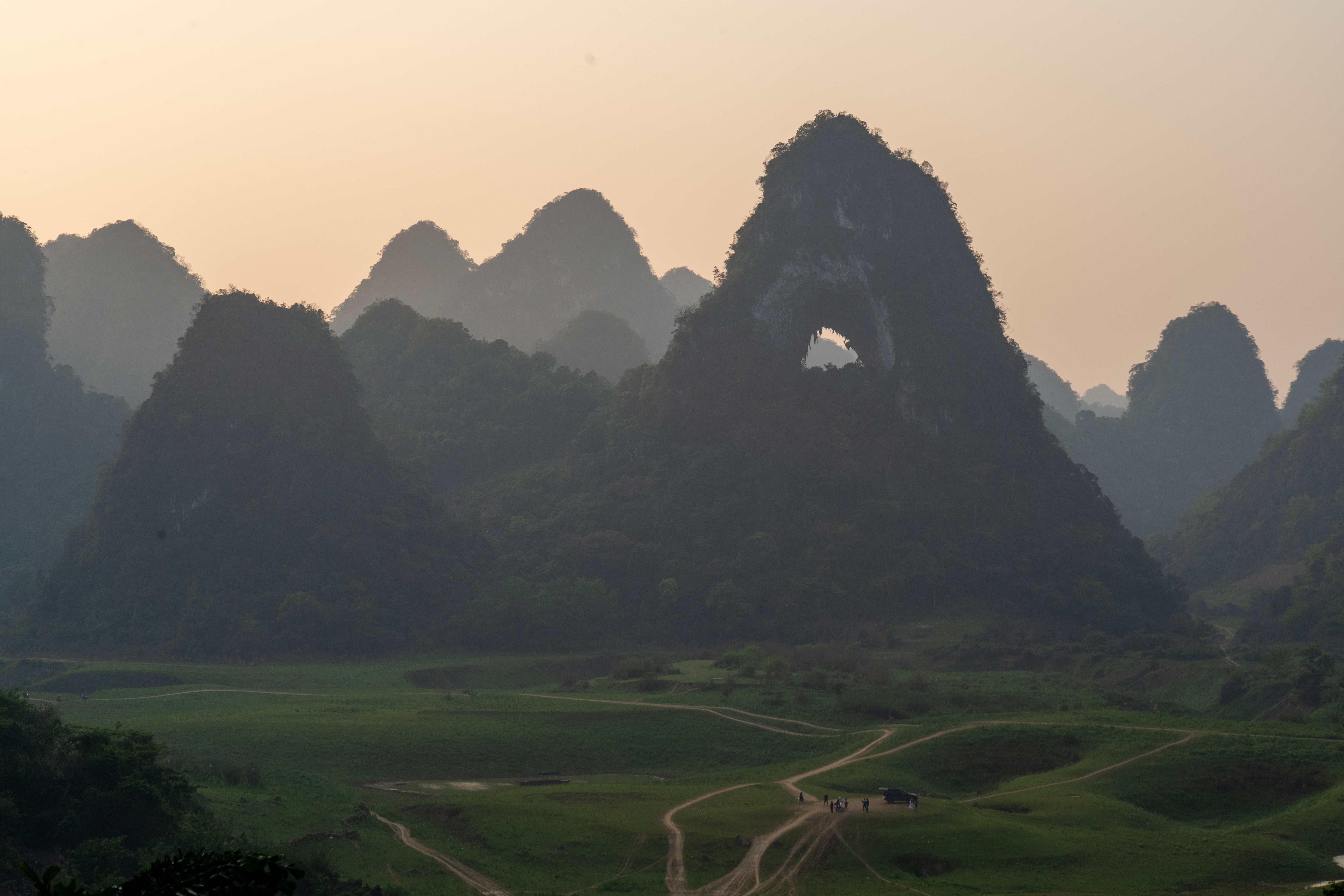 Mắt Thần — Angel Eye Mountain at golden hour, karst silhouettes layered in golden haze